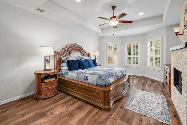 bedroom with baseboards, visible vents, a raised ceiling, wood finished floors, and a stone fireplace