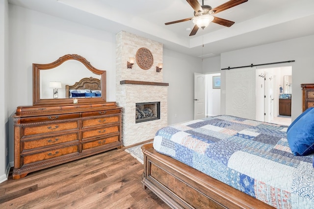 bedroom featuring a tray ceiling, a barn door, a large fireplace, connected bathroom, and wood finished floors