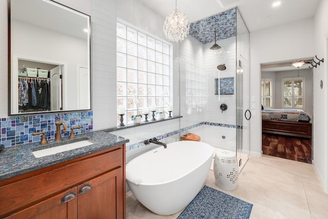 ensuite bathroom featuring tasteful backsplash, tile patterned flooring, a freestanding bath, vanity, and a shower stall