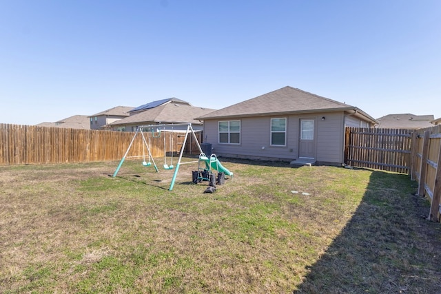 rear view of house featuring a lawn, a playground, and a fenced backyard