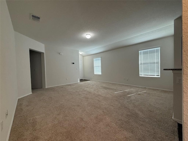 empty room featuring carpet, visible vents, a textured ceiling, and baseboards