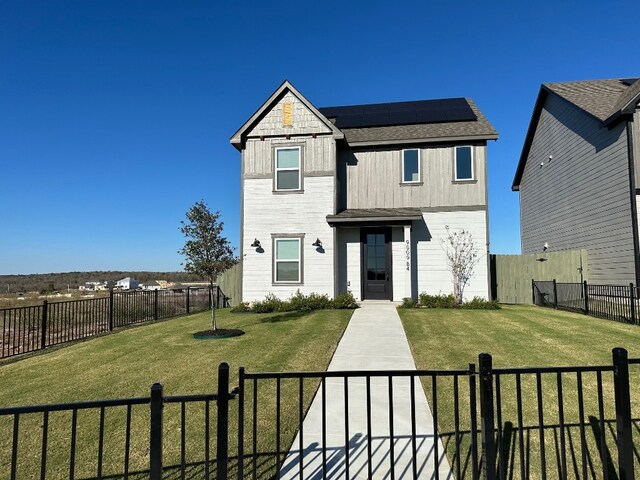 view of front facade with board and batten siding, a front yard, a fenced backyard, and roof mounted solar panels