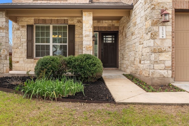 doorway to property with an attached garage, stone siding, and covered porch