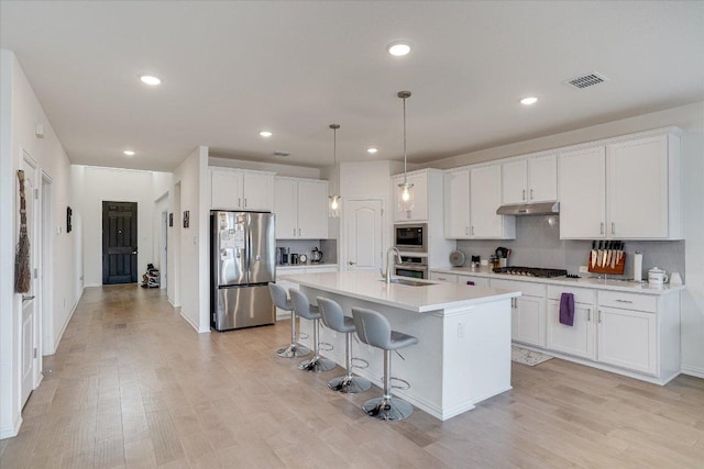 kitchen featuring under cabinet range hood, visible vents, white cabinets, appliances with stainless steel finishes, and tasteful backsplash