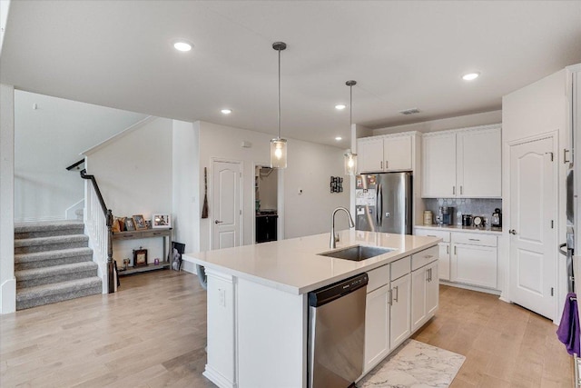 kitchen with light wood-style floors, a center island with sink, stainless steel appliances, and a sink