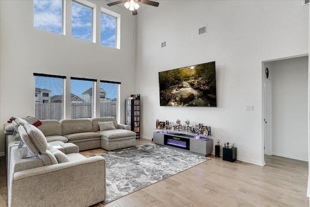 living room featuring light wood-style floors, a ceiling fan, visible vents, and a wealth of natural light