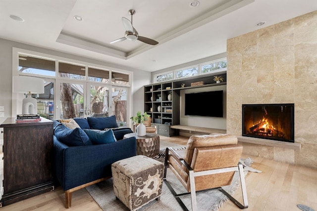 living area featuring a raised ceiling, plenty of natural light, a tiled fireplace, and wood finished floors