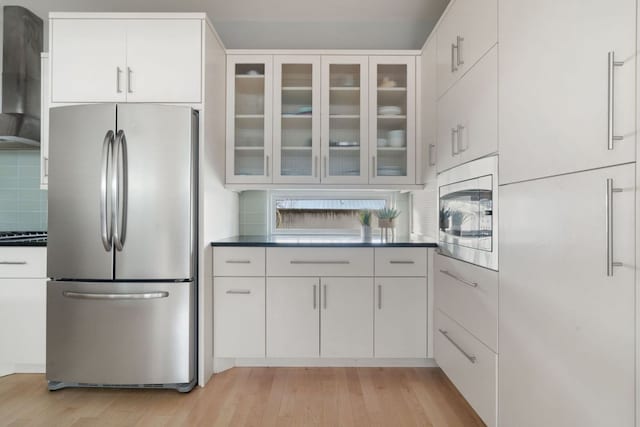 kitchen featuring appliances with stainless steel finishes, light wood-type flooring, glass insert cabinets, and backsplash