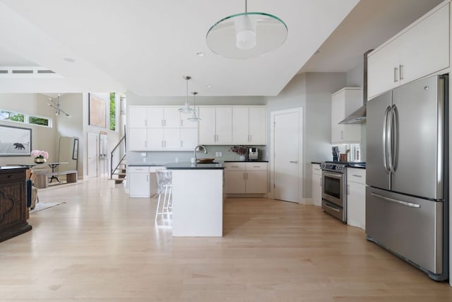 kitchen with decorative light fixtures, stainless steel appliances, dark countertops, a kitchen island with sink, and a sink