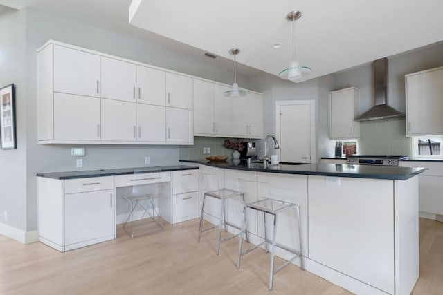 kitchen featuring a sink, white cabinets, stainless steel range with gas cooktop, wall chimney exhaust hood, and dark countertops