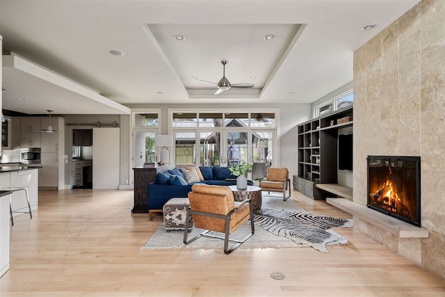 living room with built in shelves, a tray ceiling, a fireplace, light wood-style floors, and ceiling fan