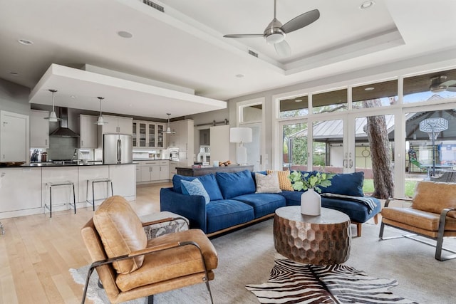 living room with ceiling fan, a tray ceiling, visible vents, and light wood-style flooring