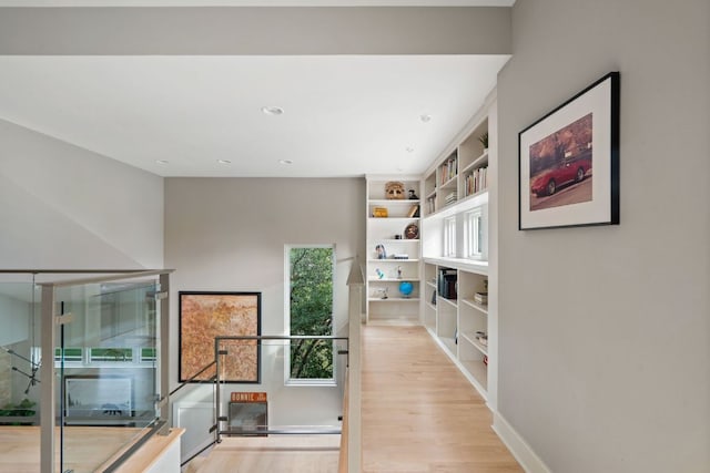 hallway featuring built in features, light wood-style flooring, and baseboards