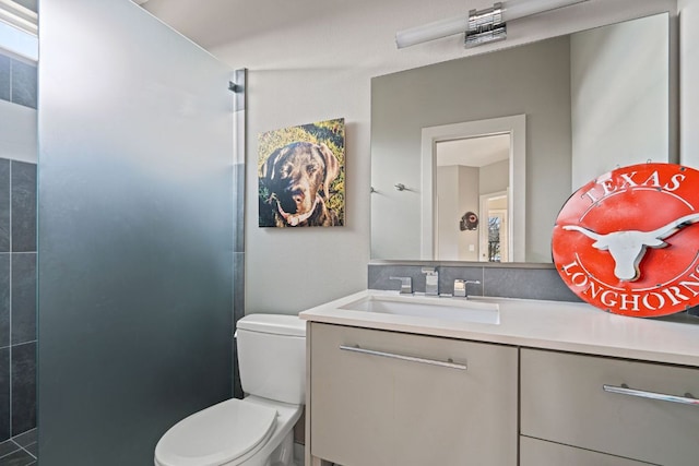 bathroom with a tile shower, vanity, and toilet