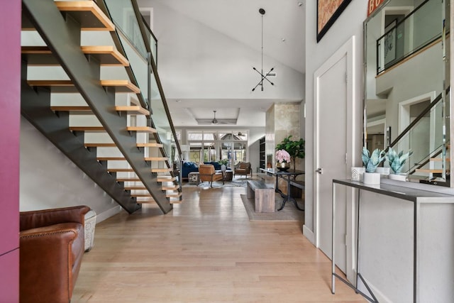 foyer entrance featuring baseboards, stairway, light wood-style floors, high vaulted ceiling, and ceiling fan with notable chandelier