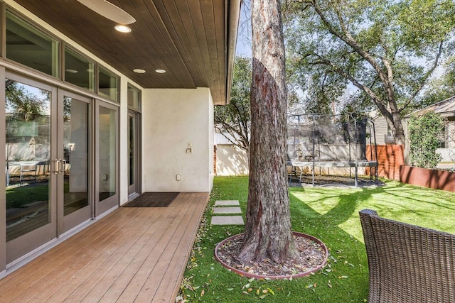 view of yard with french doors, a trampoline, fence, and a wooden deck