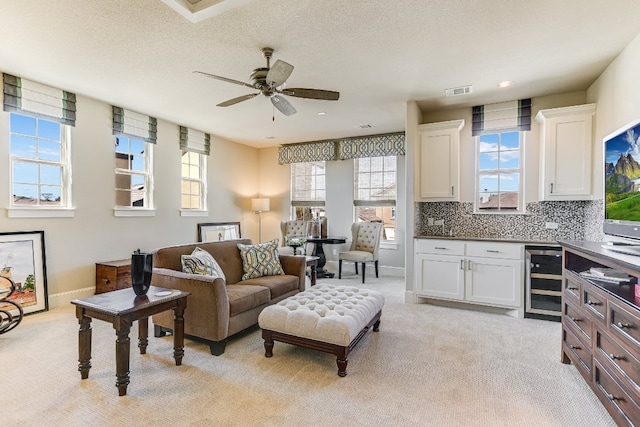 living room featuring beverage cooler, ceiling fan, light carpet, and baseboards