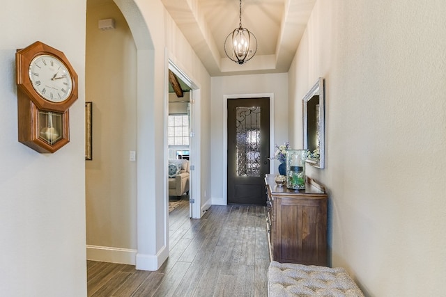 foyer with arched walkways, a notable chandelier, a raised ceiling, wood finished floors, and baseboards