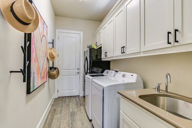 laundry room featuring cabinet space, light wood finished floors, baseboards, separate washer and dryer, and a sink