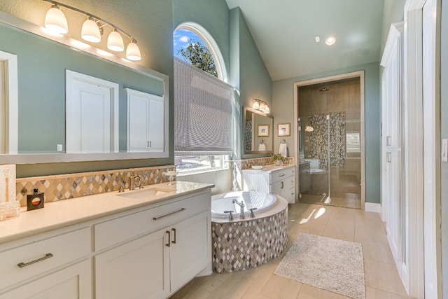 full bath with two vanities, a sink, vaulted ceiling, a shower stall, and a bath