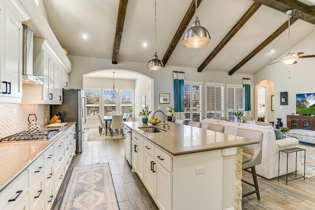 kitchen featuring arched walkways, decorative backsplash, open floor plan, stainless steel appliances, and a sink