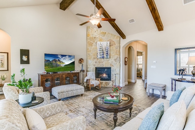 living room with visible vents, arched walkways, wood finished floors, a stone fireplace, and high vaulted ceiling