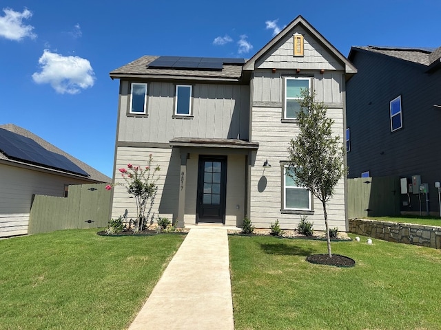 view of front of house featuring solar panels, fence, a front lawn, and board and batten siding