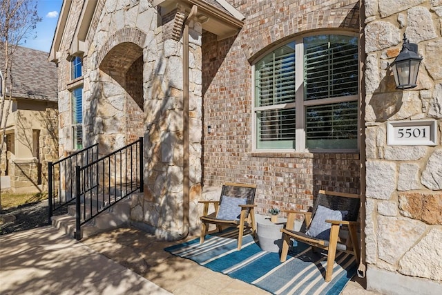 exterior space featuring stone siding, brick siding, a patio area, and a shingled roof