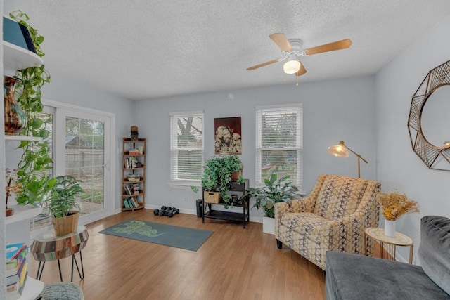 sitting room with ceiling fan, a textured ceiling, baseboards, and wood finished floors