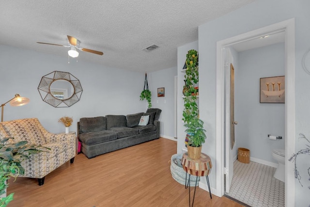 living room with visible vents, a ceiling fan, a textured ceiling, wood finished floors, and baseboards