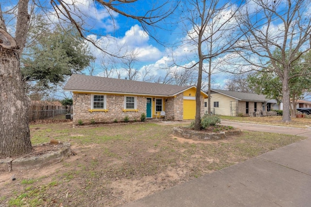 view of front of home featuring driveway, stone siding, a shingled roof, and fence