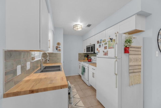 kitchen featuring white appliances, tasteful backsplash, light tile patterned floors, white cabinetry, and a sink