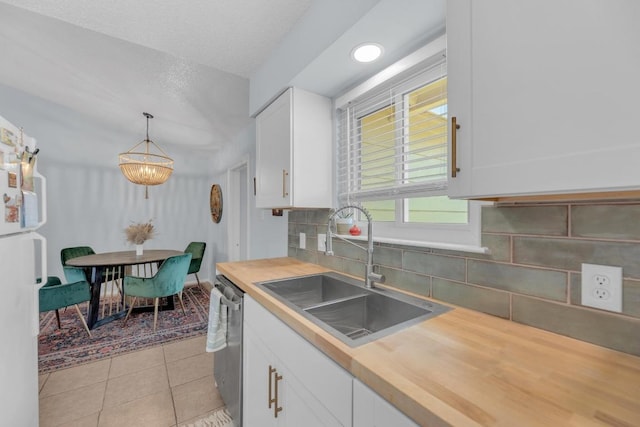 kitchen with light tile patterned floors, butcher block counters, stainless steel dishwasher, white cabinets, and a sink