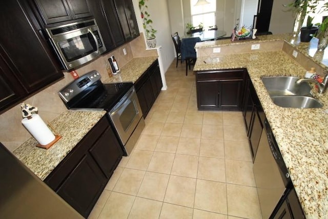 kitchen featuring light tile patterned floors, light stone counters, stainless steel appliances, a sink, and decorative backsplash