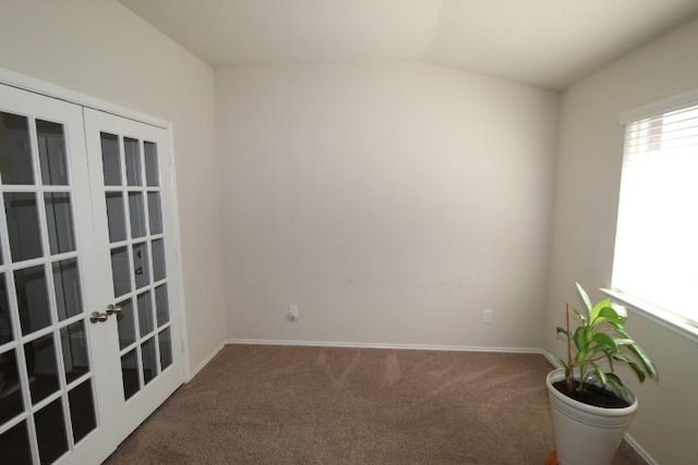 carpeted spare room featuring lofted ceiling, baseboards, and french doors