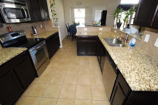 kitchen featuring light tile patterned floors, decorative backsplash, appliances with stainless steel finishes, a peninsula, and a sink