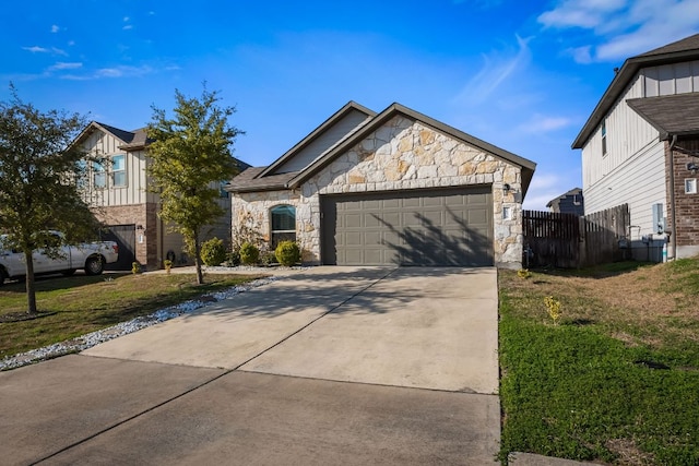 view of front of house with an attached garage, fence, stone siding, driveway, and a front lawn