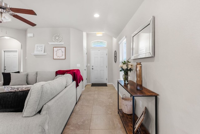 foyer entrance featuring arched walkways, light tile patterned floors, a ceiling fan, vaulted ceiling, and baseboards