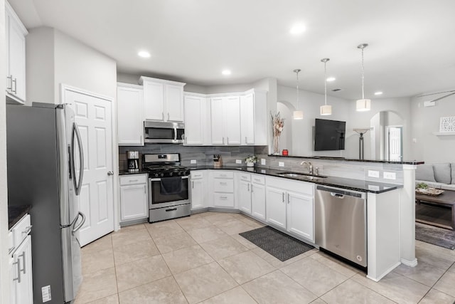 kitchen with arched walkways, stainless steel appliances, dark countertops, tasteful backsplash, and a sink