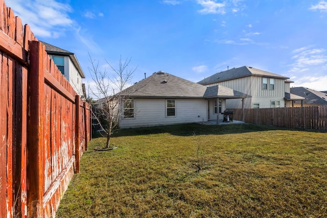 rear view of house with a fenced backyard, a shingled roof, a patio, and a yard