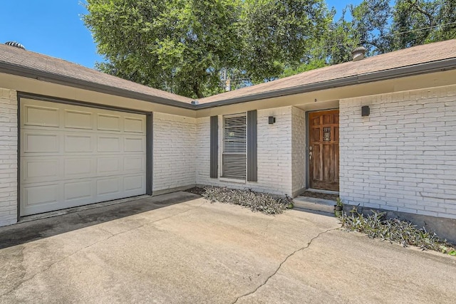 doorway to property with driveway, brick siding, and an attached garage