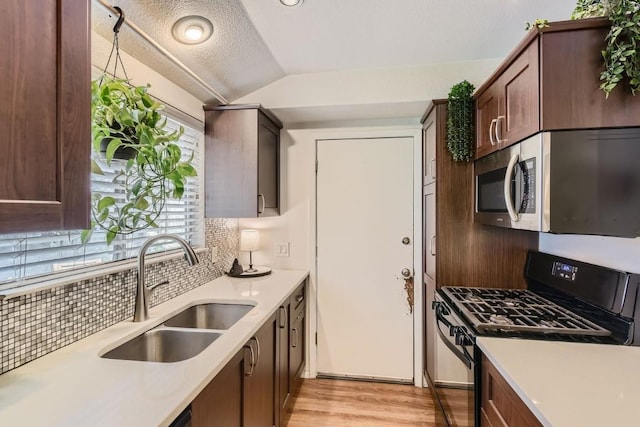 kitchen featuring a sink, vaulted ceiling, light countertops, black range with gas stovetop, and stainless steel microwave