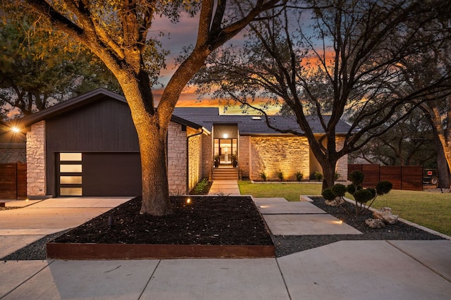 view of front facade with concrete driveway, a front yard, fence, a garage, and stone siding