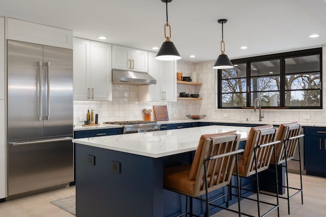 kitchen featuring decorative backsplash, a center island, blue cabinetry, stainless steel appliances, and under cabinet range hood