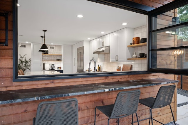 kitchen featuring open shelves, tasteful backsplash, white cabinetry, a sink, and under cabinet range hood