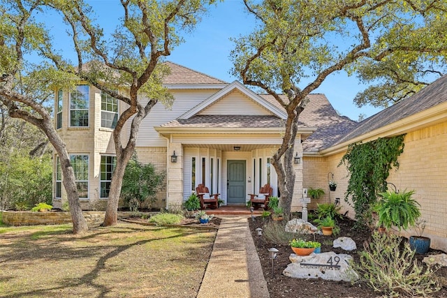 view of front of property with covered porch, brick siding, and a shingled roof