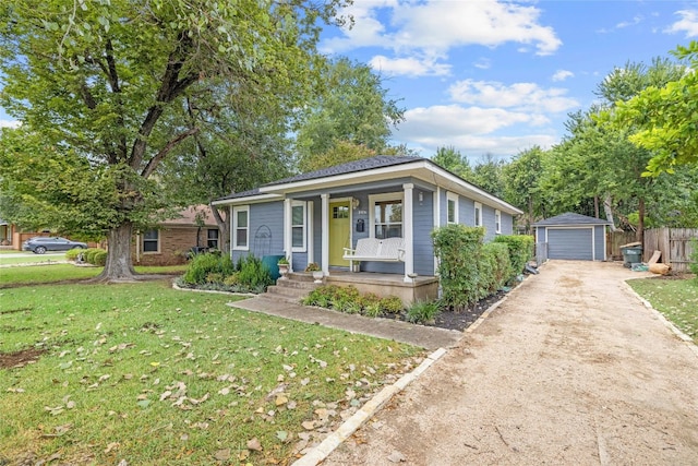 bungalow-style home featuring a garage, driveway, an outbuilding, covered porch, and a front lawn