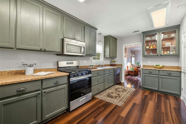 1906 Paige St, Georgetown, TX 78626 - kitchen featuring appliances with stainless steel finishes, green cabinetry, dark wood finished floors, glass insert cabinets, and decorative light fixtures