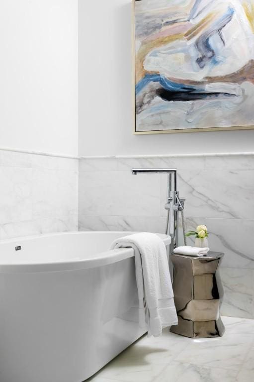 bathroom featuring marble finish floor, a soaking tub, and tile walls