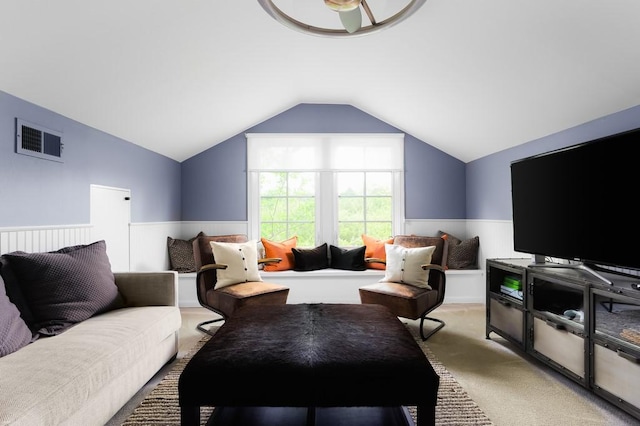 carpeted living area featuring a wainscoted wall, visible vents, and vaulted ceiling